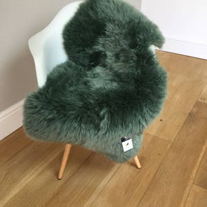 May include: A green sheepskin rug draped over a white chair with wooden legs. The rug is soft and fluffy, and the chair is a modern design.