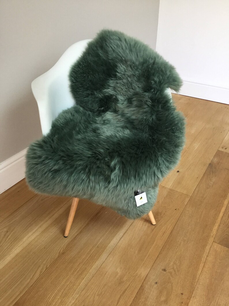 May include: A green sheepskin rug draped over a white chair with wooden legs. The rug is soft and fluffy, and the chair is a modern design.