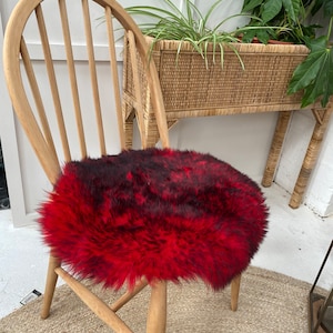 Op de afbeelding: Een rond, pluche stoelzitting van nep bont in rood en zwart. De zitting is geplaatst op een houten stoel.
