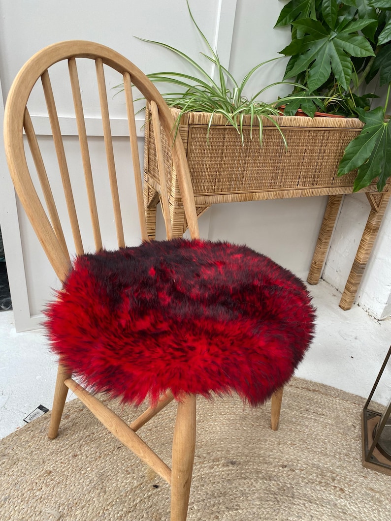 Op de afbeelding: Een rond, pluche stoelzitting van nep bont in rood en zwart. De zitting is geplaatst op een houten stoel.