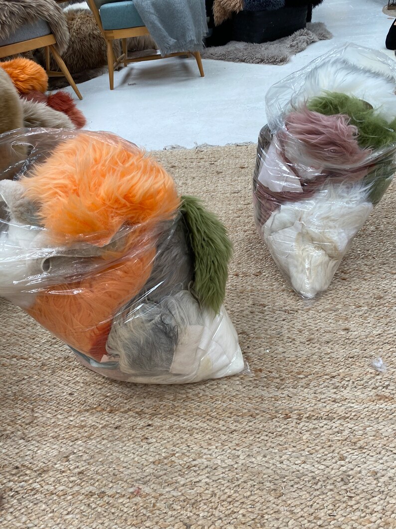 May include: Two clear plastic bags filled with various colors of faux fur. The bags are sitting on a woven rug.