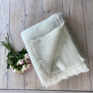 May include: A white fuzzy blanket with a fringed edge is folded on a wooden surface.