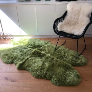 May include: A green sheepskin rug with a fluffy texture, laid out on a wooden floor. A black chair with a white sheepskin cushion is in the background.