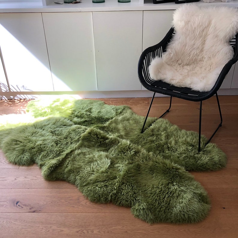 May include: A green sheepskin rug with a fluffy texture, laid out on a wooden floor. A black chair with a white sheepskin cushion is in the background.