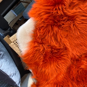 Könnte beinhalten: Eine Nahaufnahme eines leuchtend orangefarbenen Schaffellteppichs. Der Teppich ist weich und flauschig mit langen, dicken Fasern. Er ist perfekt, um jedem Raum einen Hauch von Wärme und Textur zu verleihen.