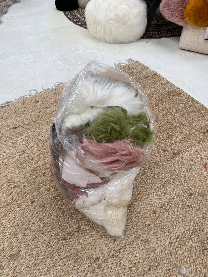 May include: A clear plastic bag filled with various colors of faux fur. The fur is white, pink, green, and brown. The bag is sitting on a woven rug.