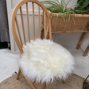 Op de afbeelding: Een houten stoel met een wit nep bont kussen. De stoel heeft een gebogen rugleuning en een ronde zitting. De stoel staat op een geweven tapijt.