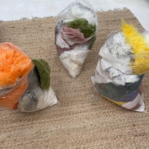 May include: Three clear plastic bags filled with different colors of faux fur. The bags are on a woven rug.