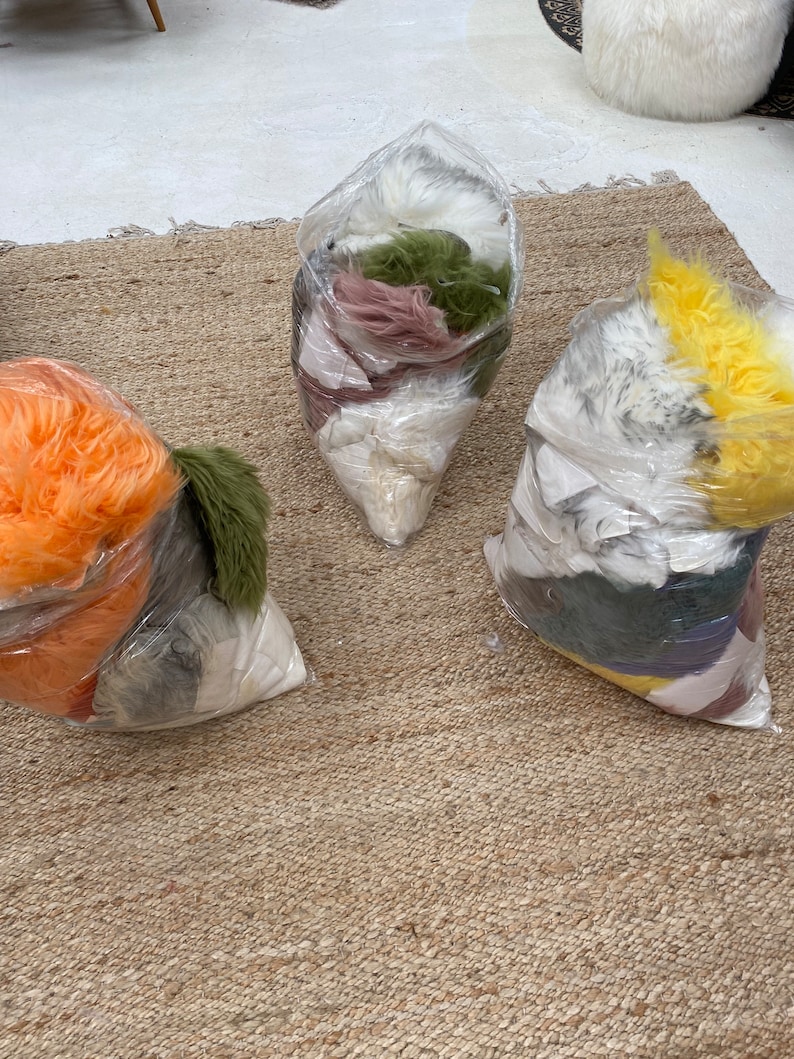 May include: Three clear plastic bags filled with different colors of faux fur. The bags are on a woven rug.