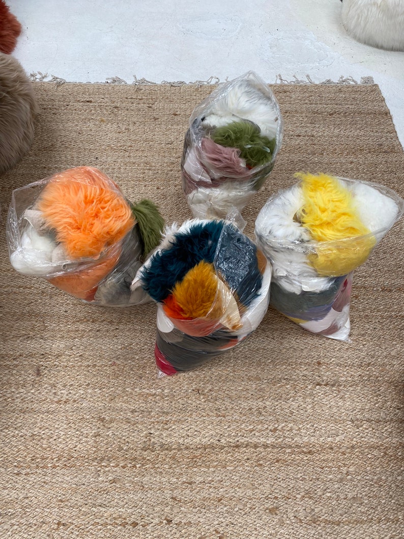 May include: Five bags of colorful faux fur, each containing different colors and textures. The bags are arranged on a light brown woven rug.