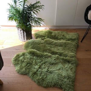 May include: A green sheepskin rug laid out on a wooden floor. The rug is made of soft, fluffy fur and is arranged in a wave-like pattern.