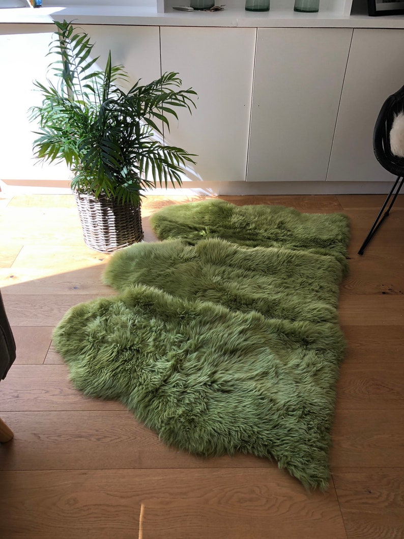 May include: A green sheepskin rug laid out on a wooden floor. The rug is made of soft, fluffy fur and is arranged in a wave-like pattern.