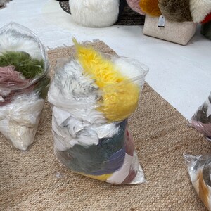 May include: A close-up of a large plastic bag filled with various colors of faux fur. The bag is sitting on a woven rug.