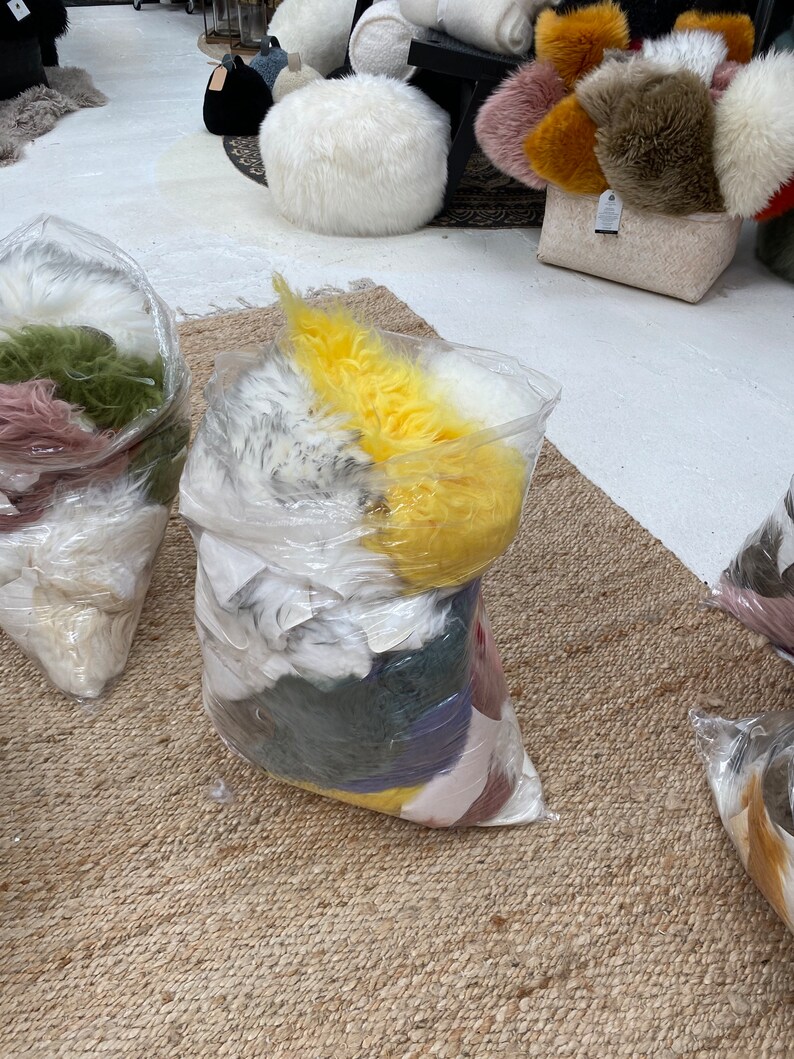 May include: A close-up of a large plastic bag filled with various colors of faux fur. The bag is sitting on a woven rug.