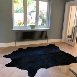 May include: A black cowhide rug on a light wood floor with a gray radiator and a window with a view of trees in the background.