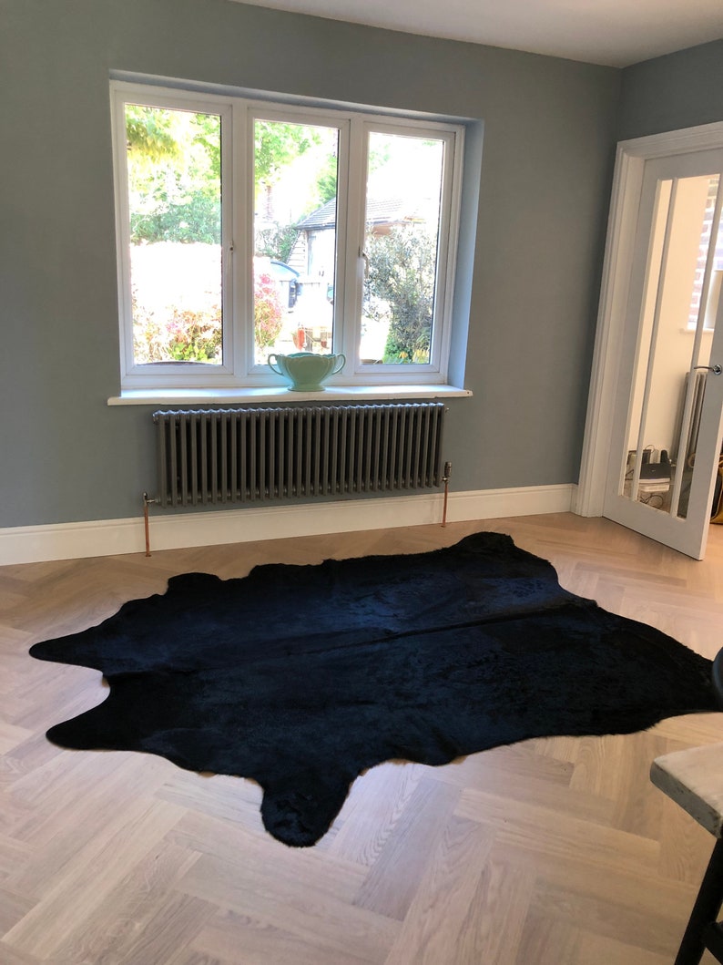May include: A black cowhide rug on a light wood floor with a gray radiator and a window with a view of trees in the background.