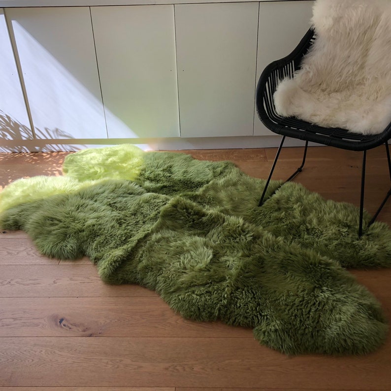May include: A green and yellow sheepskin rug with long, fluffy fur. The rug is laid out on a wooden floor.