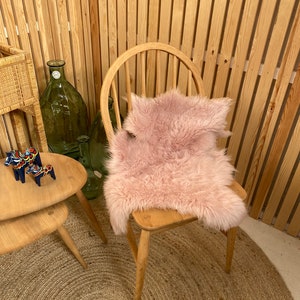 May include: A pink faux fur rug sits on a wooden chair with a slatted wood wall in the background. The chair is in front of a round jute rug.