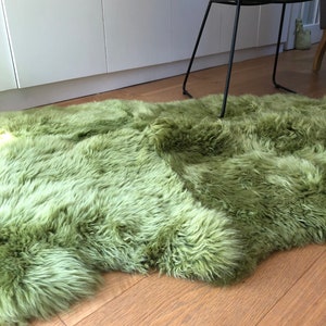 May include: A soft, green sheepskin rug with long, fluffy fur. The rug is laid out on a wooden floor.