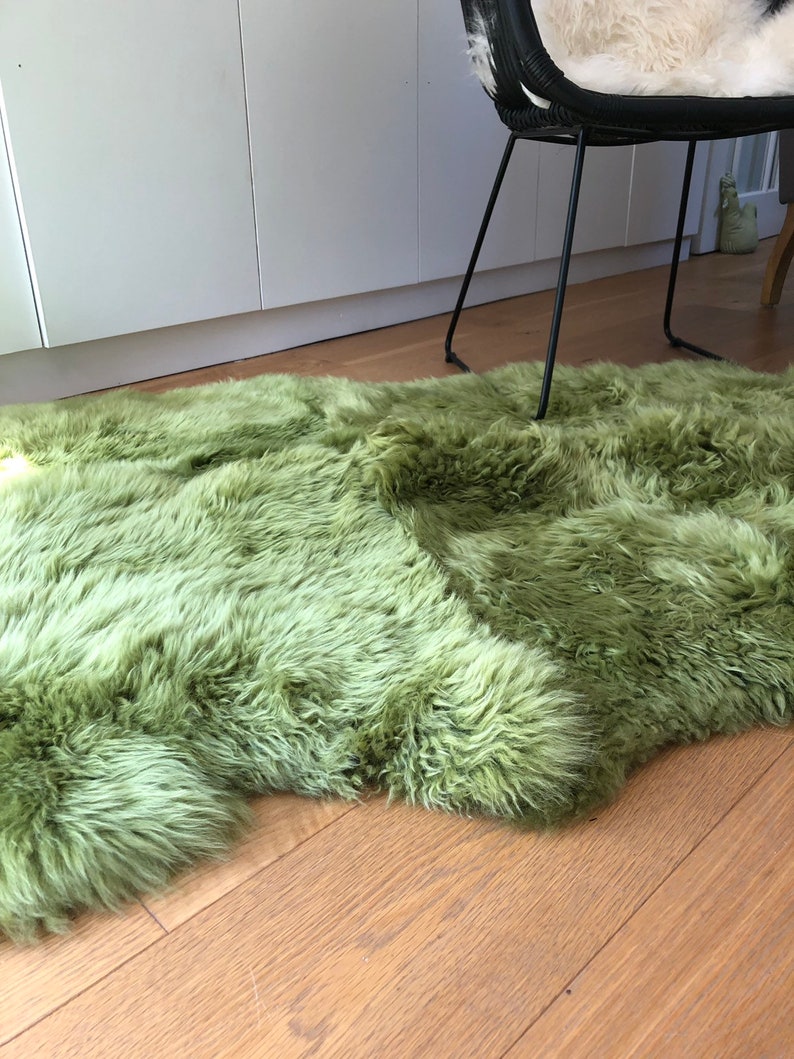May include: A soft, green sheepskin rug with long, fluffy fur. The rug is laid out on a wooden floor.