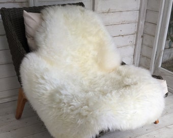 May include: A white sheepskin rug draped over a wicker chair with a white cushion. The rug is soft and fluffy, and the chair is made of natural materials.