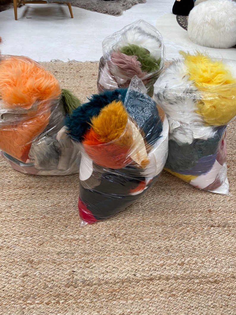 May include: Five plastic bags filled with colorful faux fur. The bags are on a woven rug.