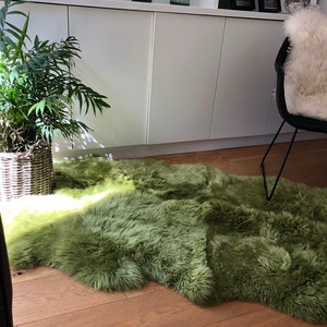 May include: A soft, green sheepskin rug with a light green gradient. The rug is laid out on a wooden floor in a living room setting.