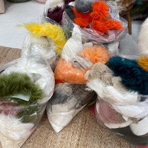 May include: A variety of colorful faux fur pieces are packaged in clear plastic bags. The fur is in shades of orange, yellow, green, pink, white, and gray.