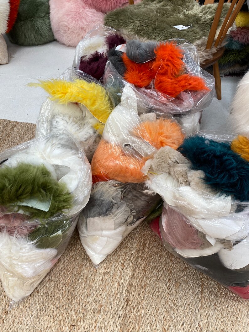 May include: A variety of colorful faux fur pieces are packaged in clear plastic bags. The fur is in shades of orange, yellow, green, pink, white, and gray.