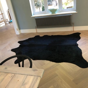 May include: A black cowhide rug on a light wood herringbone floor in a room with a gray radiator and a window.