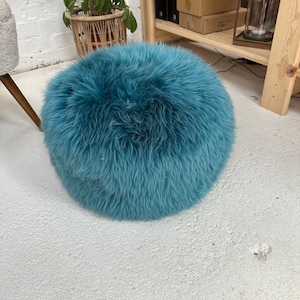 Pode incluir: Um pufe redondo e felpudo de cor azul turquesa. O pufe é feito de um material macio e felpudo e é perfeito para adicionar um toque de conforto e estilo a qualquer cômodo.