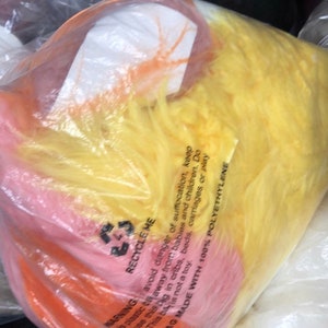 May include: A close-up of a plastic bag filled with colorful, fluffy stuffing. The bag is labeled "Recycle Me" and has a warning to avoid danger of suffocation. The bag is made with 100% polyethylene.