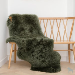 May include: A plush, green sheepskin rug draped over a wooden bench with a criss-cross back.