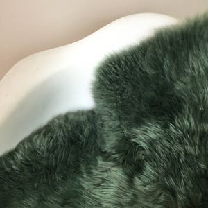 May include: A soft, plush, green sheepskin rug. The rug is laid out on a white, curved surface.
