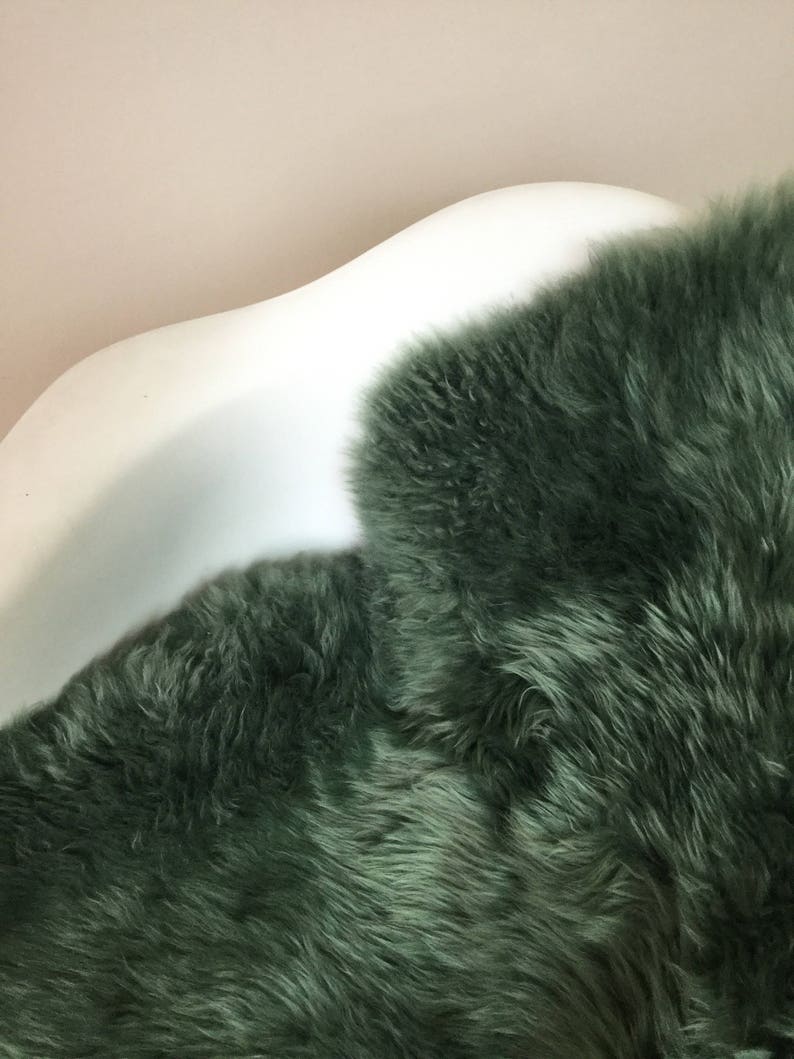 May include: A soft, plush, green sheepskin rug. The rug is laid out on a white, curved surface.
