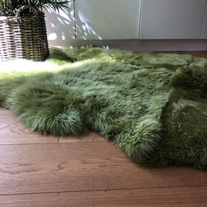 May include: A soft, green faux fur rug with a long pile. The rug is laid out on a wooden floor.