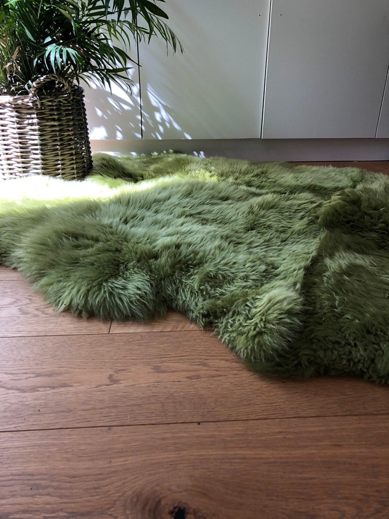 May include: A soft, green faux fur rug with a long pile. The rug is laid out on a wooden floor.