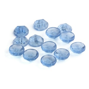 Puede incluir: Un grupo de botones de plástico facetados de color azul claro. Los botones están esparcidos sobre un fondo blanco.