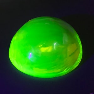Puede incluir: Un objeto de vidrio verde lima brillante y redondeado. El objeto tiene una superficie lisa y está iluminado sobre un fondo oscuro. El color es un verde vibrante y brillante.