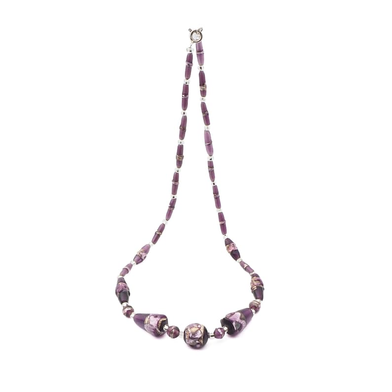 May include: A purple beaded necklace with a silver clasp. The necklace features a variety of purple beads, including cylindrical and round shapes. The beads have a marbled appearance with gold and white accents.