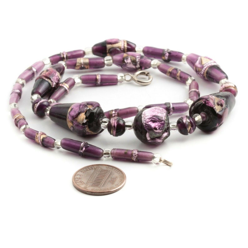 Puede incluir: Un collar artesanal con una variedad de cuentas de vidrio moradas. El collar incluye cuentas grandes de color morado oscuro con detalles dorados, cuentas moradas m&aacute;s peque&ntilde;as y cuentas transparentes. El collar mide aproximadamente 46 cm de largo.