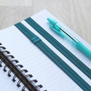 A deep cyan elastic band to carry a pen on your notebook
