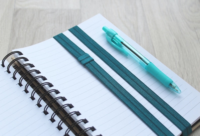 A deep cyan elastic band to carry a pen on your notebook