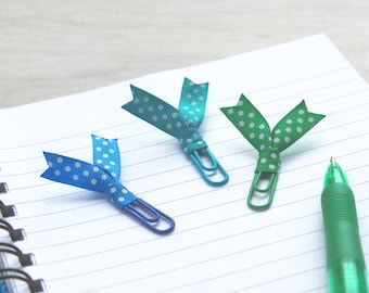 May include: Three colorful paper clips with polka dot ribbon accents. The clips are blue, green, and turquoise. A green pen is also in the image.