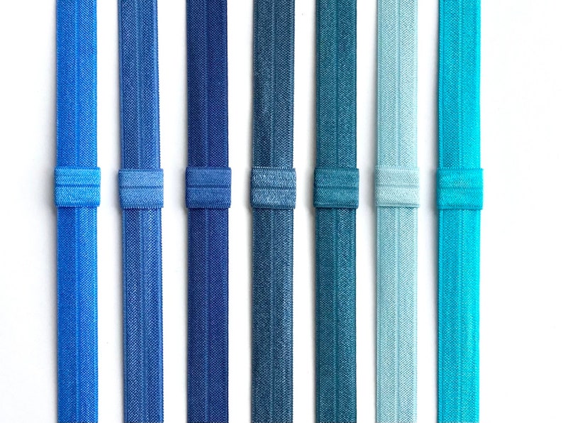 May include: Eight hair ties in various shades of blue, teal, and light blue. The hair ties are made of a stretchy, textured material.