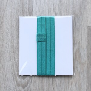 May include: Two teal elastic hair ties in a clear plastic package on a wooden background.