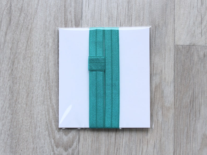 May include: Two teal elastic hair ties in a clear plastic package on a wooden background.