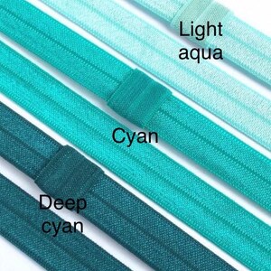 May include: Four different shades of blue elastic hair ties, from light aqua to deep cyan. The hair ties are arranged in a row, with the lightest shade at the top and the darkest shade at the bottom. The hair ties are all made of the same material and have a smooth, shiny finish.