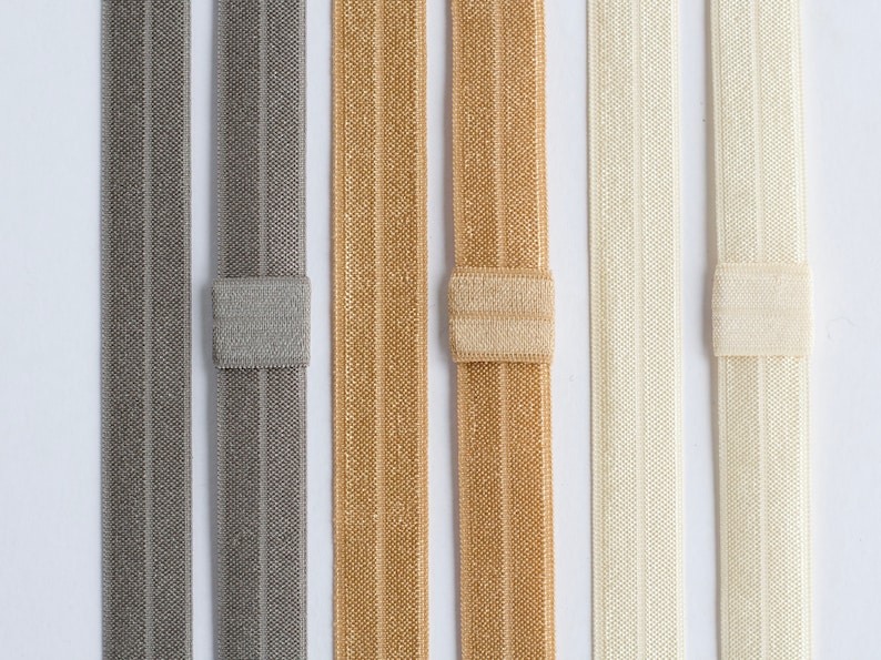May include: Five different colors of elastic hair ties, each with a different color and texture. The hair ties are arranged in a row from left to right, with the gray hair tie on the left and the white hair tie on the right.