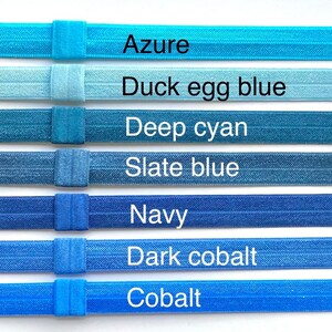 May include: Seven different shades of blue elastic hair ties, from light azure to dark cobalt. The hair ties are arranged in a row from lightest to darkest, with the color names written below each one.
